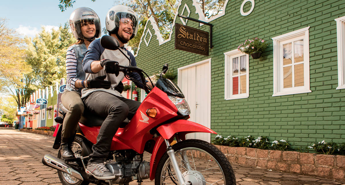 Piloto iniciante sorrindo com garupa em moto Honda vermelha