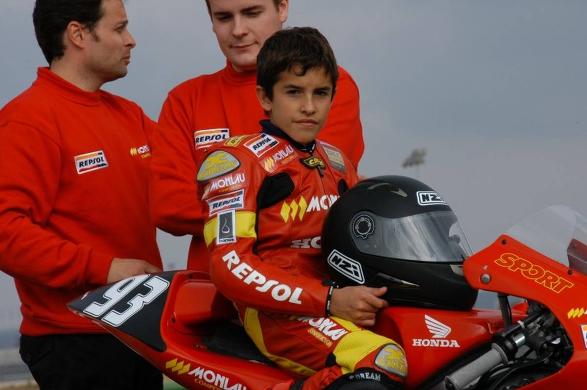 Piloto Marc Marquez em cima de uma moto Honda quando criança, com o capacete apoiado no tanque