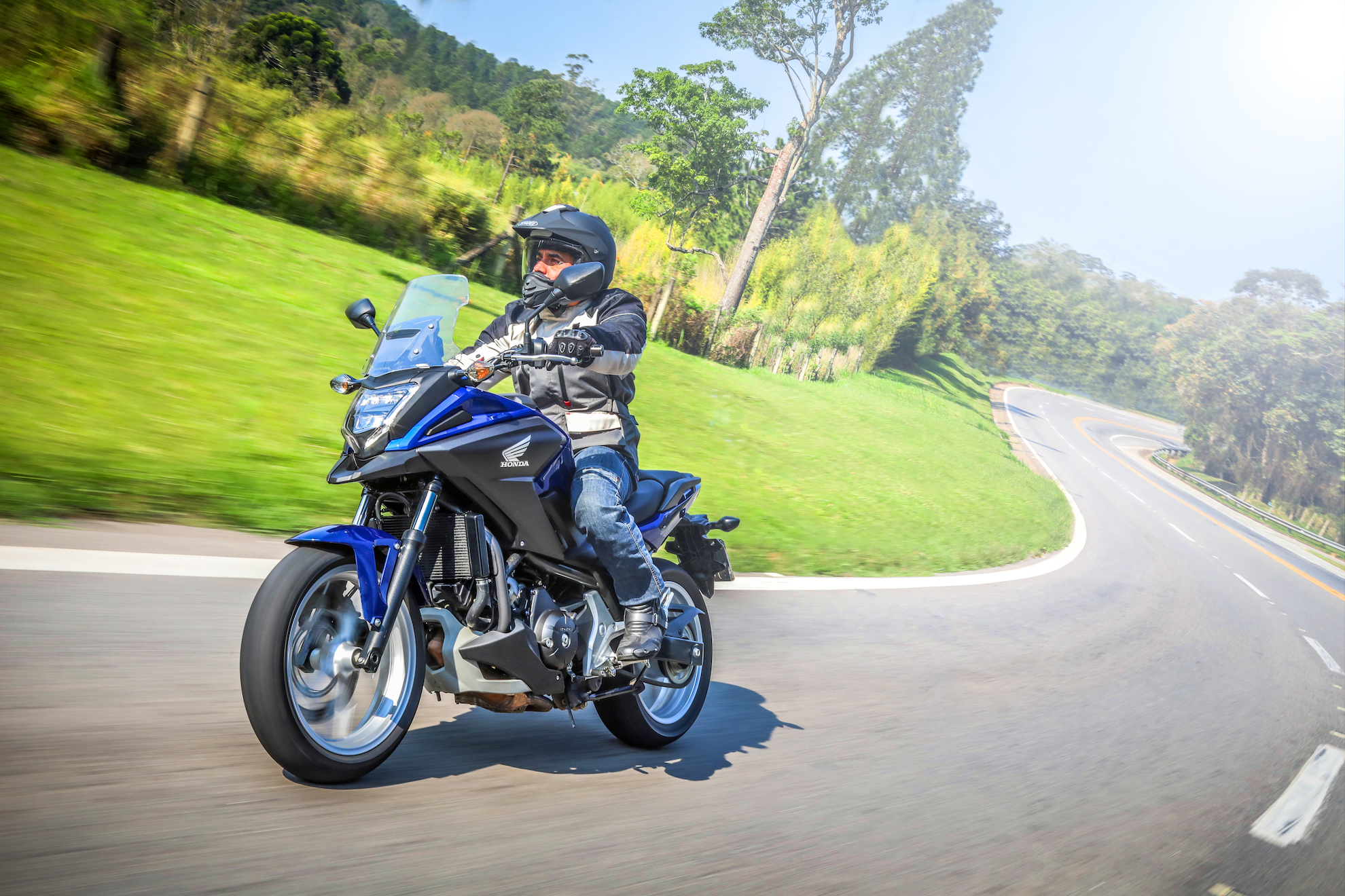 Motociclista em sua Honda NC 750X Azul pilotando na estrada fazendo curva para a esquerda