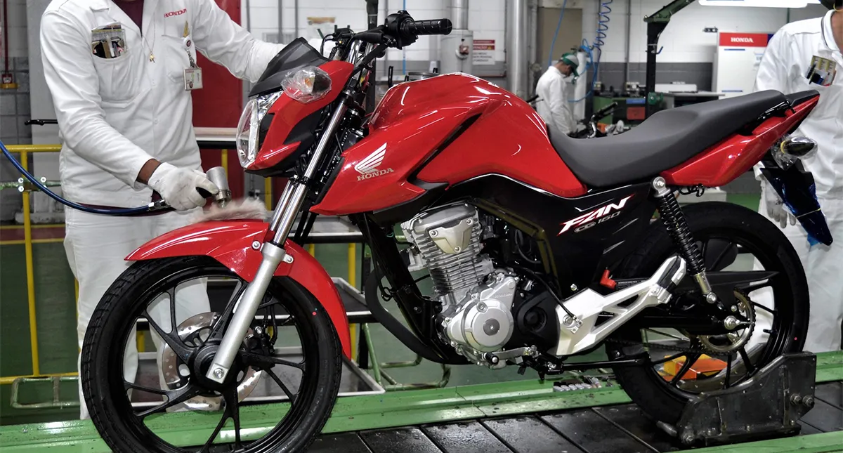 Colaborador na fábrica pitandando uma moto Honda CG 160 Fan vermelha