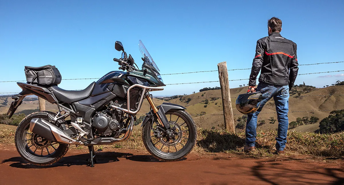 Piloto ao lado de sua motocicleta Honda CB 500X admirando paisagem de vale