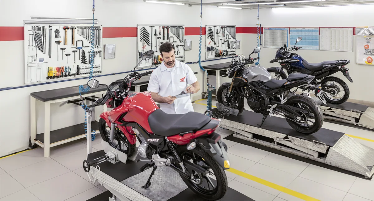 Concessionária Honda - Colaborador fazendo cheklist de uma moto honda vermelha com outras duas motos aguardando vistoria