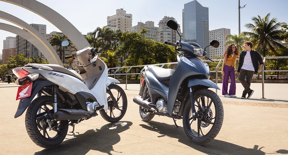 Homem e mulher ao fundo conversando e mais afrente as motocicletas honda biz 125 azul marinho e branca estcionadas