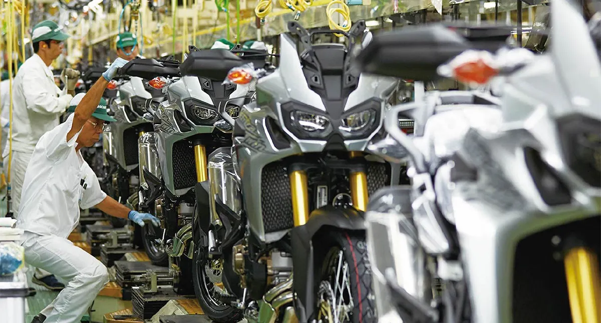 Funcionários trabalhando na linha de montagem de motocicletas Honda, com várias motos alinhadas em processo de fabricação.
